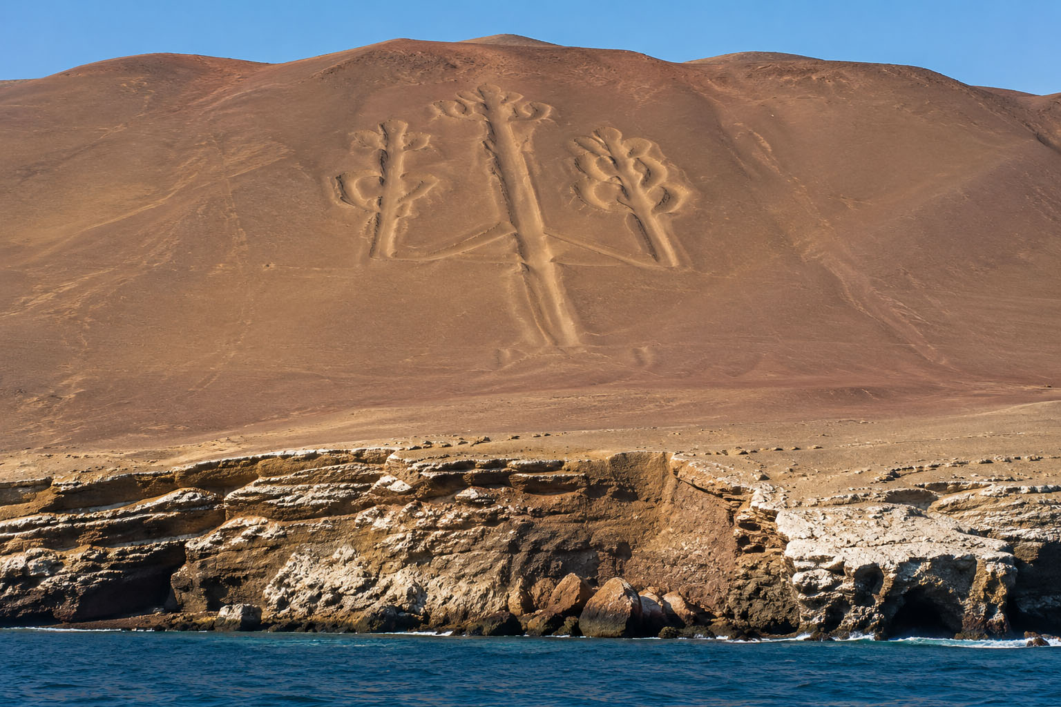 Coastal view of the Paracas Candelabra geoglyph cut into the desert hillside above the sea on the Paracas Peninsula in Peru.